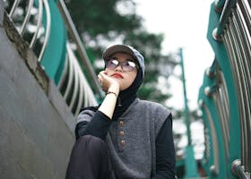 Modern Muslim woman in hijab and glasses posing outdoors on stairs in Banten, Indonesia.