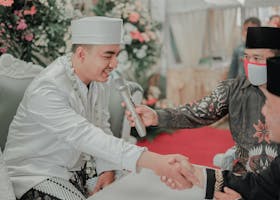 Groom in traditional attire shaking hands during wedding ceremony with floral decor.